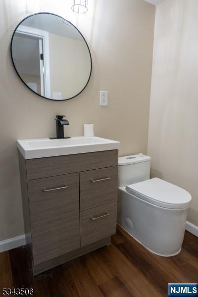 half bathroom featuring baseboards, toilet, wood finished floors, and vanity