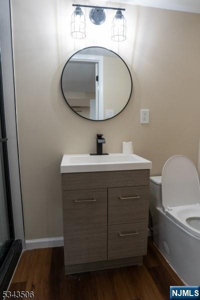 bathroom featuring baseboards, toilet, wood finished floors, and vanity