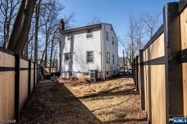 rear view of house featuring central air condition unit, fence, and a chimney