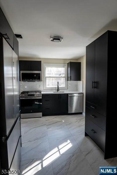 kitchen with a sink, marble finish floor, appliances with stainless steel finishes, and dark cabinetry