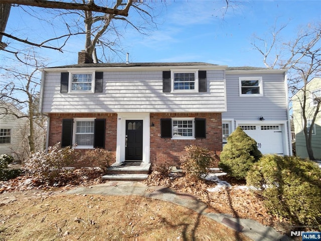 colonial home with a garage, brick siding, and a chimney