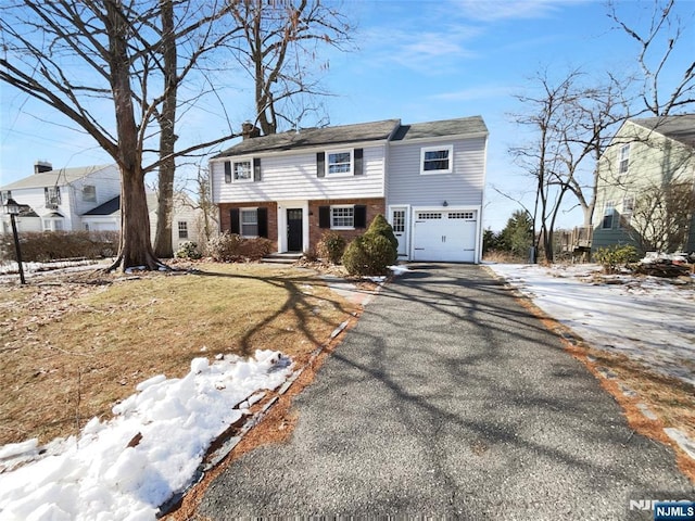 view of front of house with driveway, brick siding, an attached garage, and a chimney