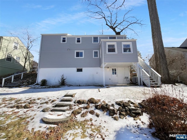 snow covered house featuring central AC unit and stairs