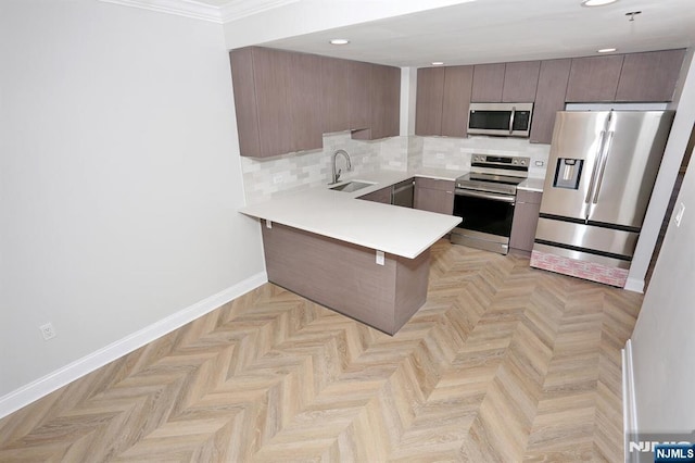 kitchen featuring tasteful backsplash, appliances with stainless steel finishes, a peninsula, light countertops, and baseboards