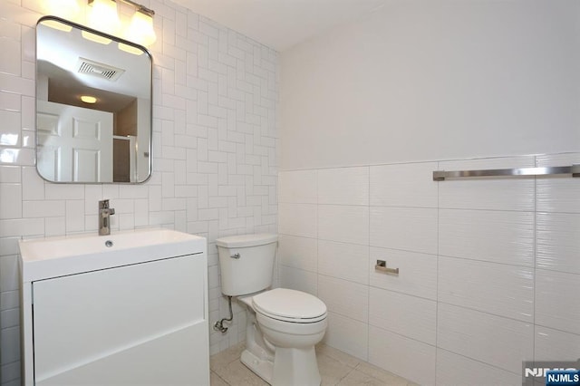 bathroom with visible vents, toilet, vanity, tile patterned floors, and tile walls