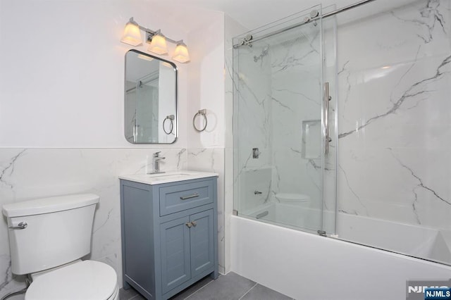 full bath featuring vanity, a wainscoted wall, shower / bath combination with glass door, tile walls, and toilet