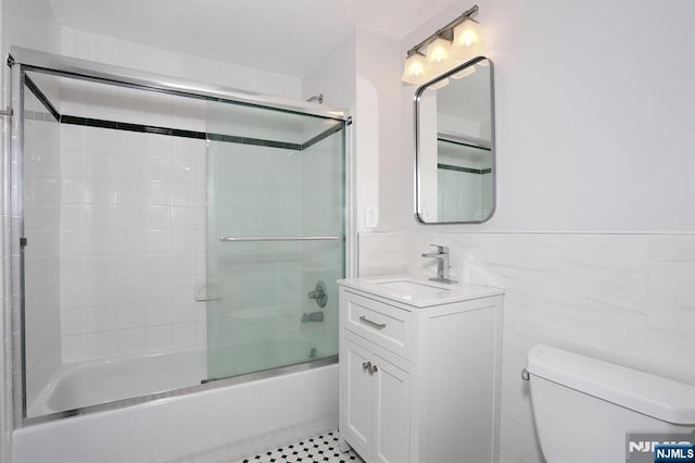 bathroom with vanity, tile walls, toilet, and combined bath / shower with glass door