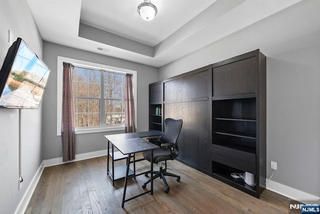 office space featuring a wealth of natural light, baseboards, a raised ceiling, and dark wood-style floors