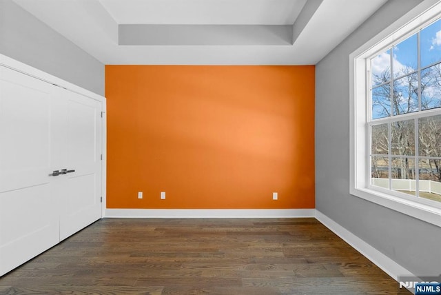 spare room featuring a tray ceiling, baseboards, and dark wood finished floors