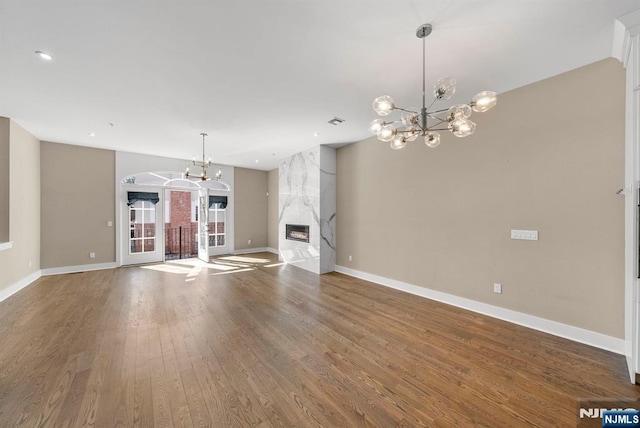 unfurnished living room featuring a high end fireplace, a notable chandelier, baseboards, and wood finished floors