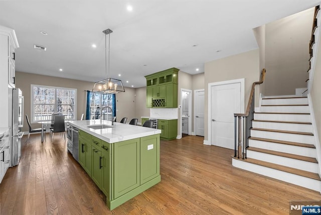 kitchen with light countertops, green cabinets, wood-type flooring, and a sink