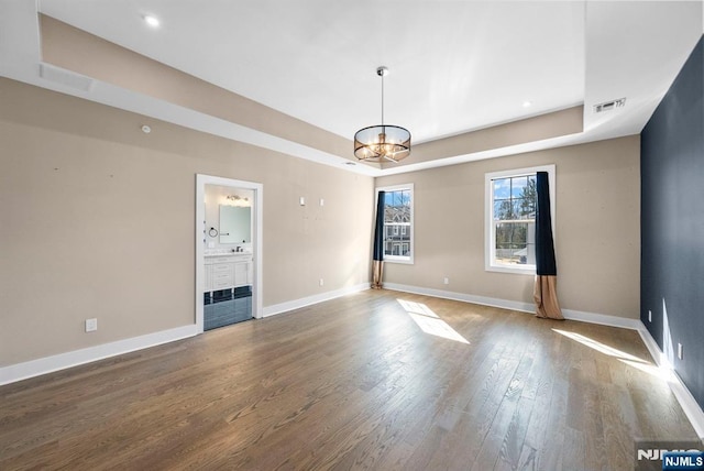 interior space featuring a raised ceiling, a notable chandelier, wood finished floors, and visible vents