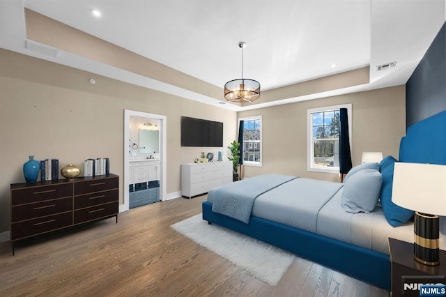 bedroom featuring visible vents, a raised ceiling, an inviting chandelier, and wood finished floors