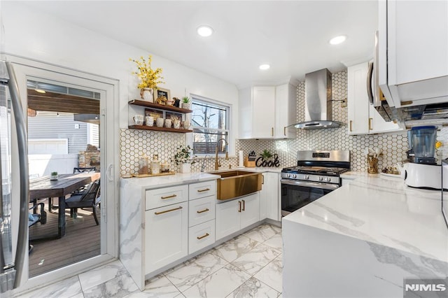 kitchen with wall chimney range hood, light stone counters, decorative backsplash, stainless steel gas stove, and a sink