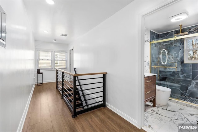 hallway featuring wood finished floors, an upstairs landing, visible vents, and baseboards