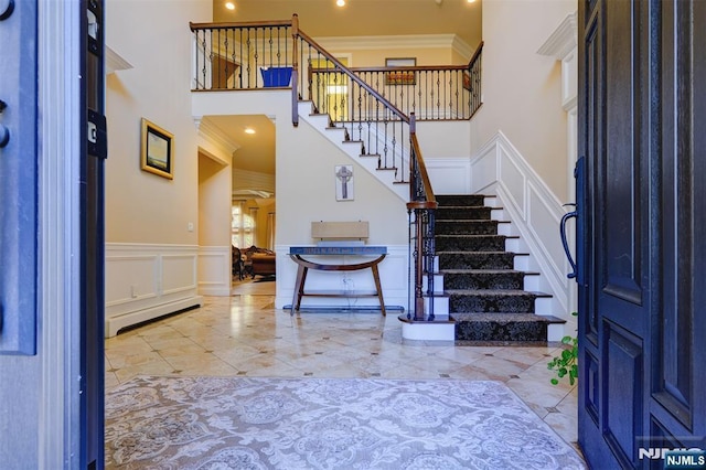 tiled foyer entrance featuring a baseboard radiator, a towering ceiling, ornamental molding, and a decorative wall