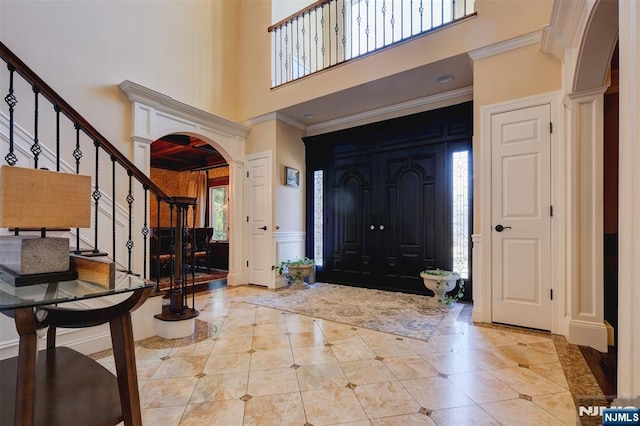 foyer entrance with ornamental molding, stairway, arched walkways, a high ceiling, and decorative columns