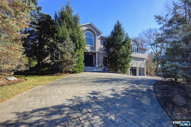 view of property hidden behind natural elements featuring decorative driveway, a garage, and stucco siding