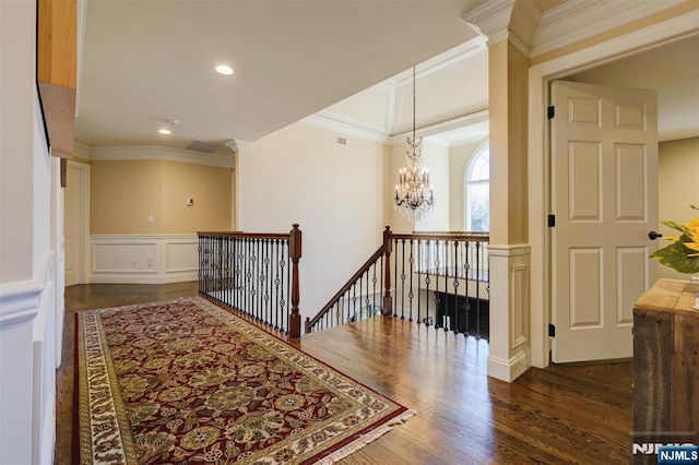 hall with an upstairs landing, ornamental molding, wood finished floors, a decorative wall, and a chandelier