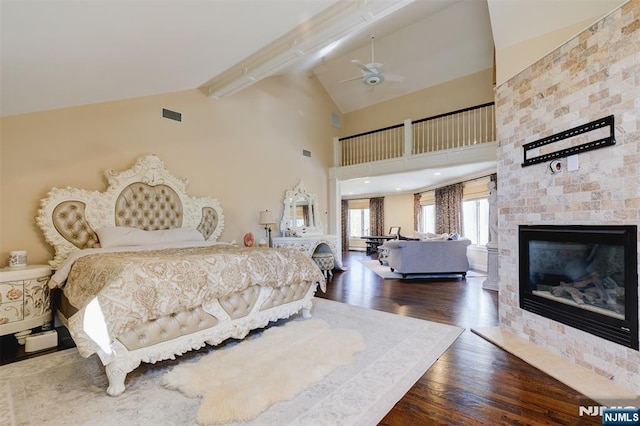 bedroom with wood finished floors, visible vents, high vaulted ceiling, beam ceiling, and a glass covered fireplace