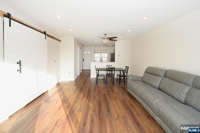 living area with light wood finished floors, recessed lighting, a ceiling fan, and a barn door