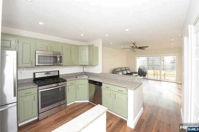 kitchen with a sink, a peninsula, appliances with stainless steel finishes, and green cabinetry