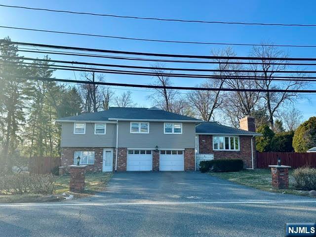 view of front of property featuring brick siding, fence, a chimney, a garage, and driveway