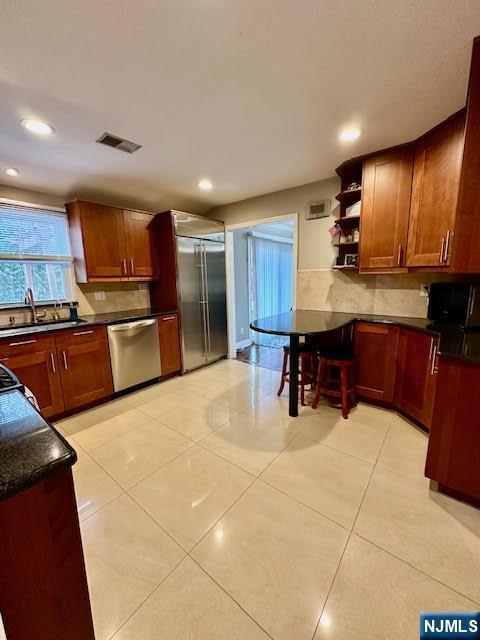 kitchen with visible vents, a sink, dark countertops, stainless steel appliances, and decorative backsplash