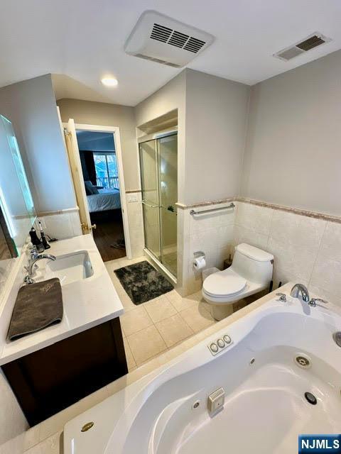 ensuite bathroom featuring toilet, a tub with jets, visible vents, and a stall shower