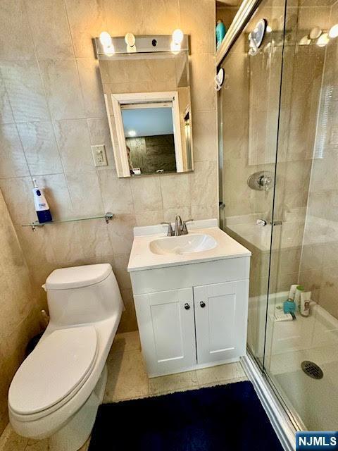 bathroom featuring vanity, tile walls, a shower stall, and toilet