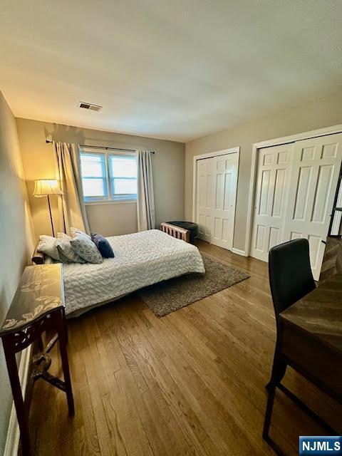 bedroom with visible vents, baseboards, multiple closets, and dark wood-style flooring