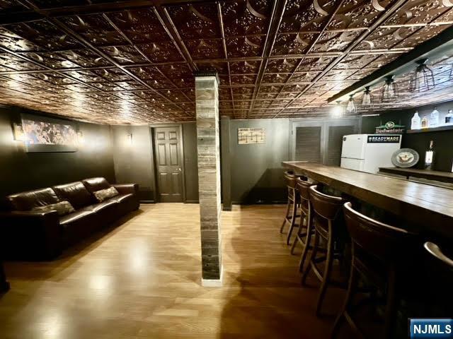 bar with fridge, a dry bar, wood finished floors, and an ornate ceiling