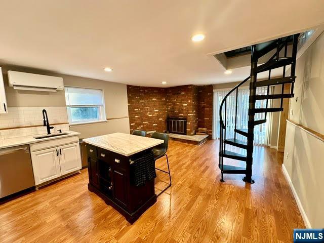 kitchen featuring a wall unit AC, light wood-style flooring, a sink, dishwasher, and tasteful backsplash