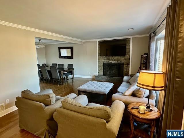 living area featuring a fireplace, crown molding, baseboards, and wood finished floors