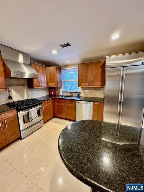 kitchen featuring visible vents, a sink, backsplash, appliances with stainless steel finishes, and wall chimney exhaust hood