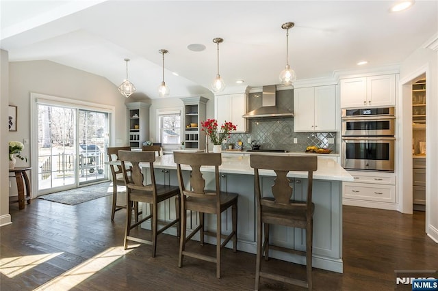 kitchen with dark wood-style flooring, backsplash, wall chimney range hood, and vaulted ceiling