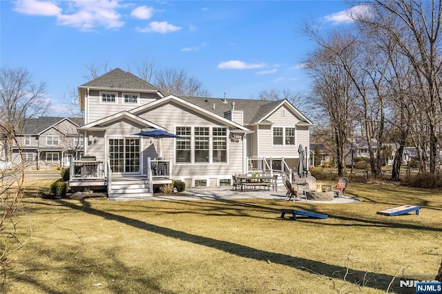 rear view of house featuring a deck, an outdoor fire pit, a yard, roof with shingles, and a patio area