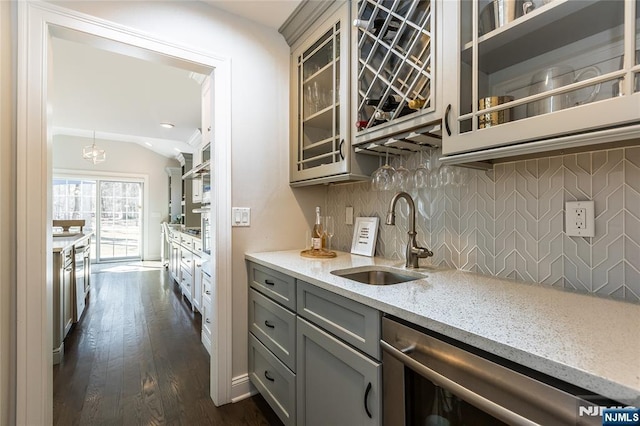 kitchen with tasteful backsplash, gray cabinetry, light stone countertops, dishwasher, and a sink