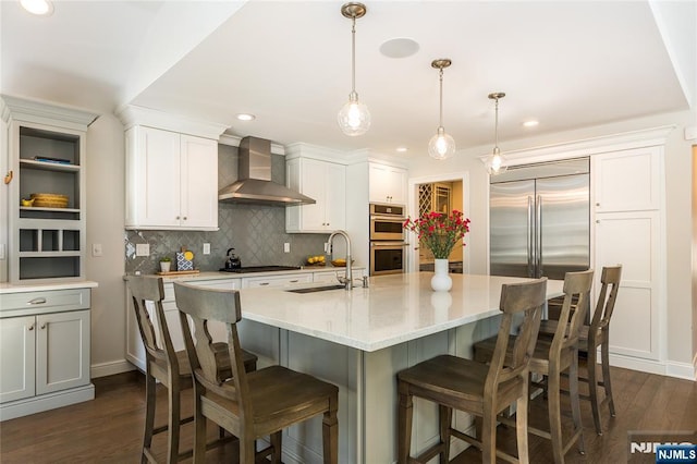 kitchen with a sink, decorative backsplash, dark wood-type flooring, appliances with stainless steel finishes, and wall chimney exhaust hood