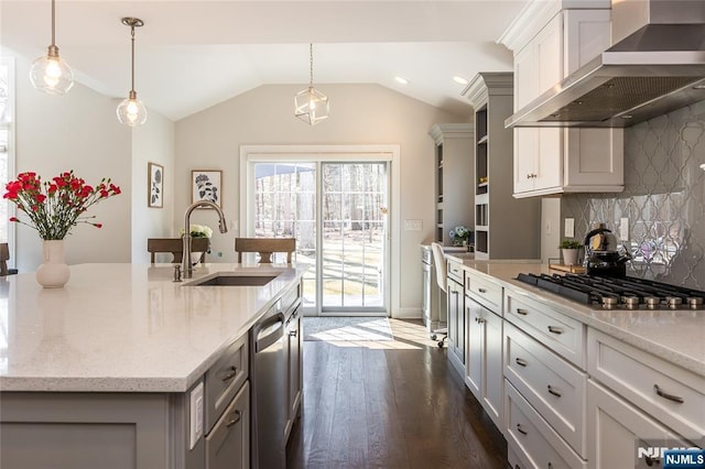 kitchen featuring a center island with sink, a sink, appliances with stainless steel finishes, wall chimney exhaust hood, and lofted ceiling