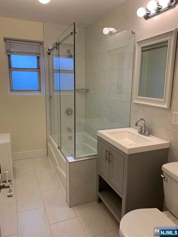 full bathroom with marble finish floor, toilet, vanity, and bath / shower combo with glass door