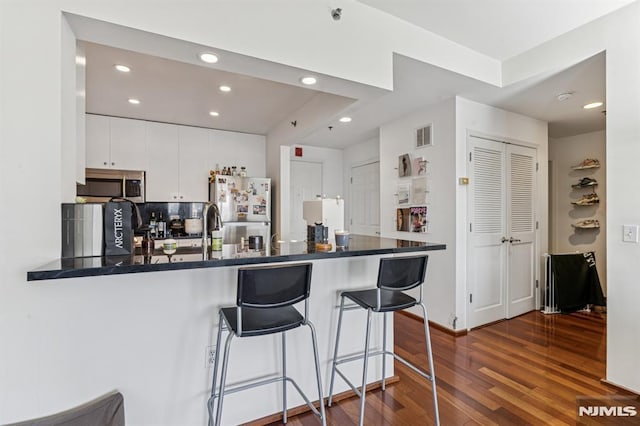 kitchen featuring dark countertops, appliances with stainless steel finishes, a peninsula, and dark wood finished floors