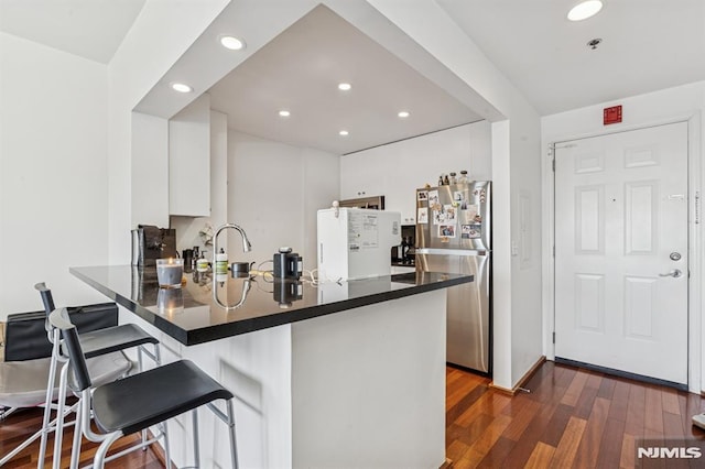 kitchen featuring dark wood-type flooring, dark countertops, white cabinetry, freestanding refrigerator, and a peninsula