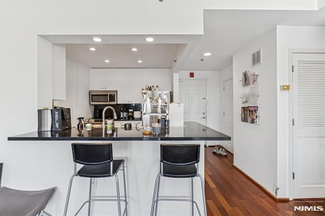 kitchen with a breakfast bar area, a peninsula, dark wood-type flooring, appliances with stainless steel finishes, and dark countertops