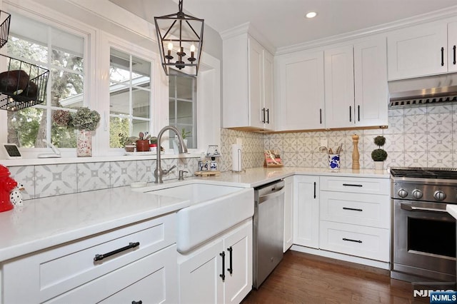 kitchen featuring light countertops, range hood, appliances with stainless steel finishes, white cabinets, and a sink