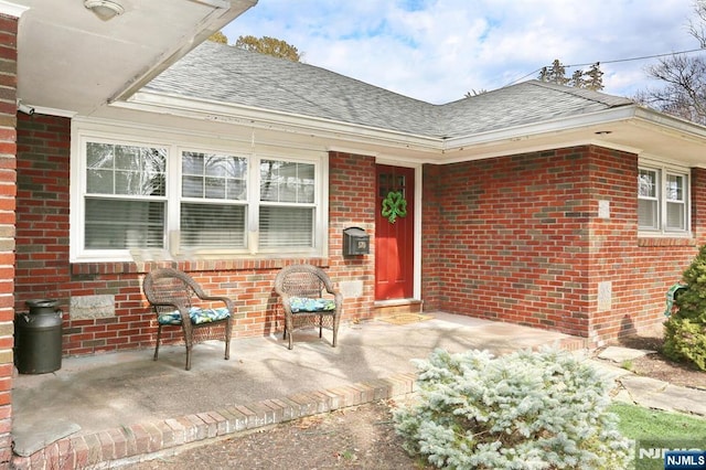 view of exterior entry with brick siding and a shingled roof