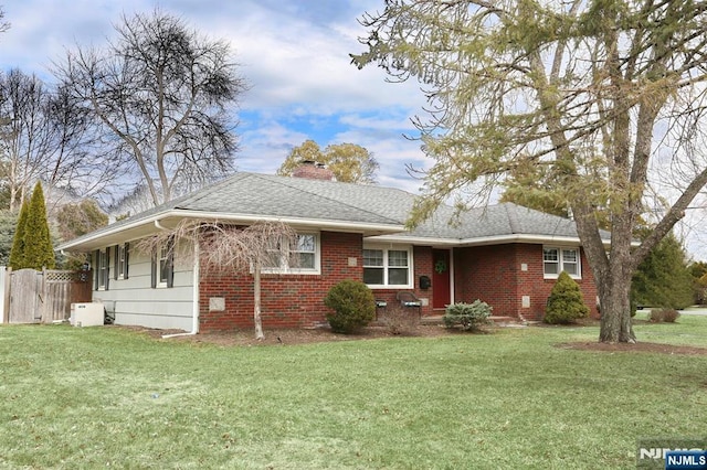 ranch-style house featuring a front yard, fence, roof with shingles, and a chimney