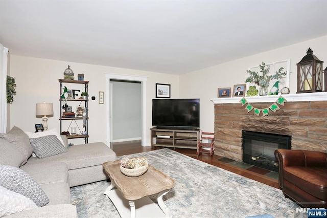 living room with baseboards, a stone fireplace, and wood finished floors