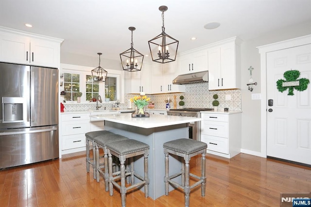 kitchen with under cabinet range hood, appliances with stainless steel finishes, white cabinetry, and a kitchen breakfast bar