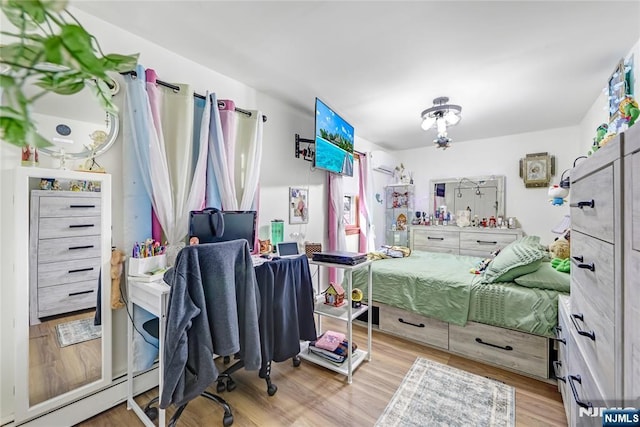 bedroom with a baseboard radiator, an AC wall unit, and wood finished floors